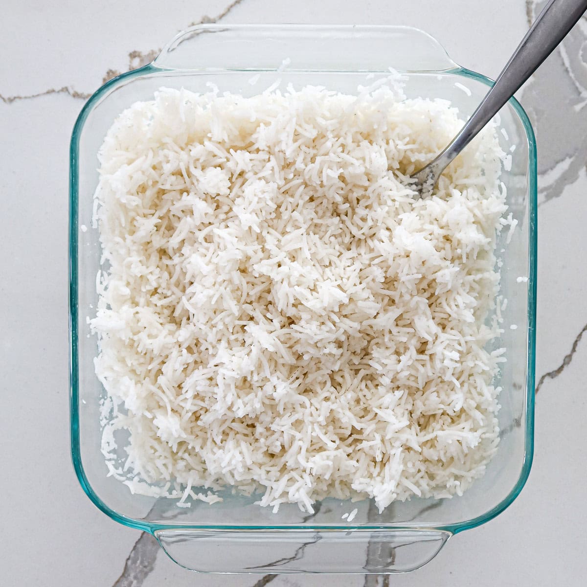 Cooked white rice fluffed with fork in baking dish.