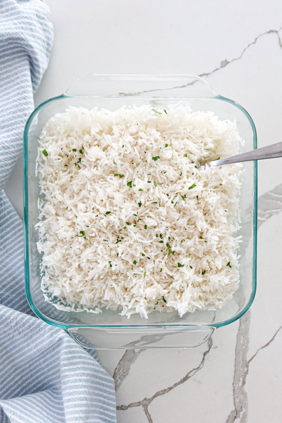 Cooked, fluffy white rice in a baking dish topped with a sprinkle of cilantro.