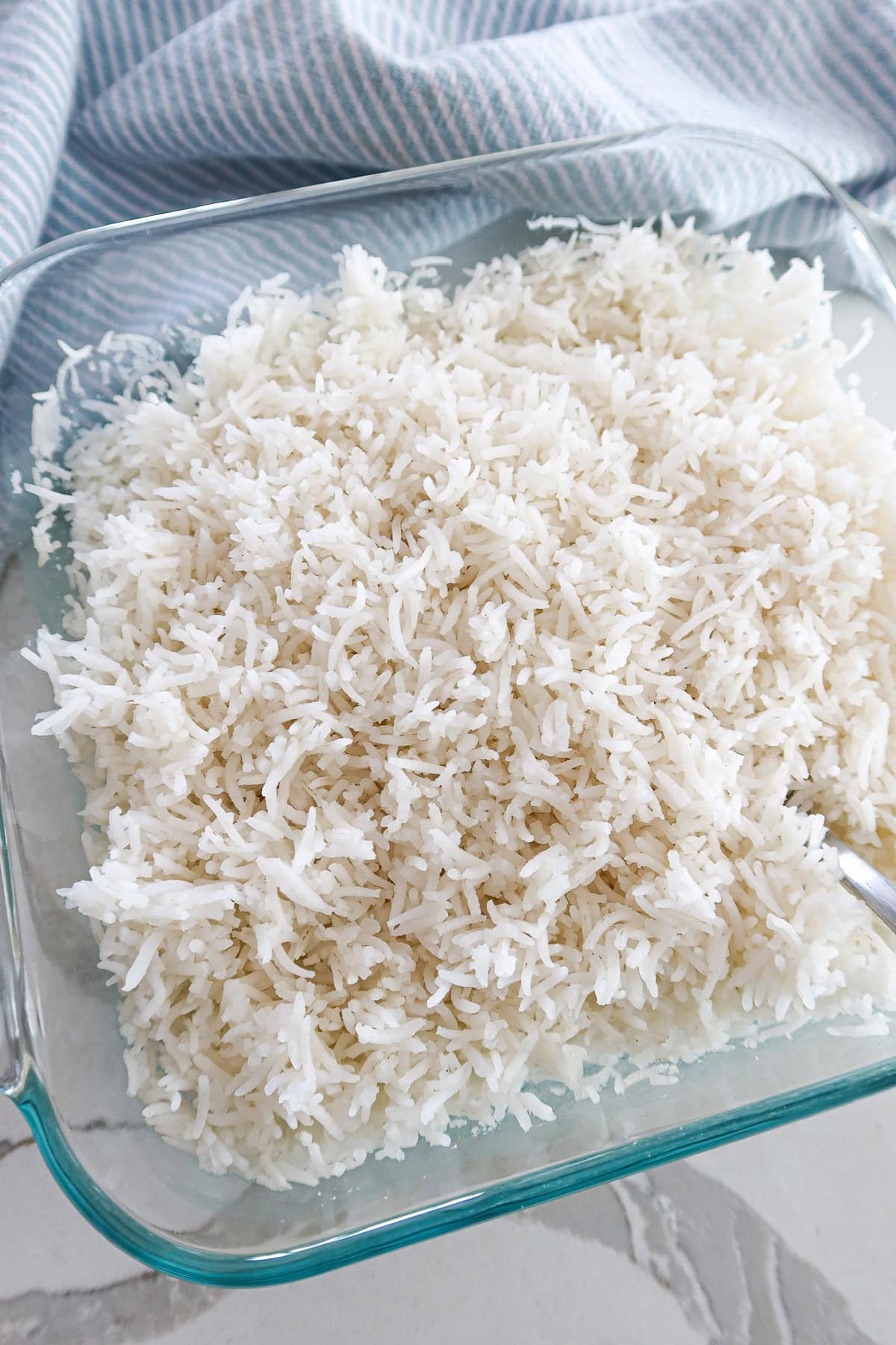 Cooked white rice fluffed with fork in baking dish.