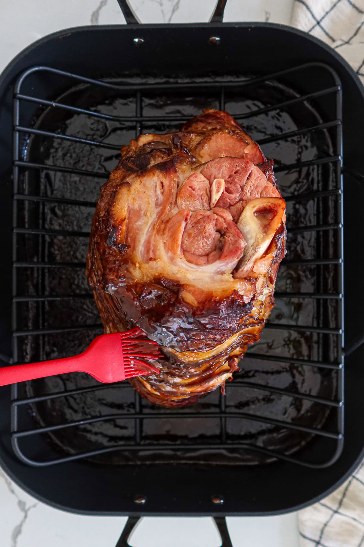 Overhead view of spiral-sliced ham in a roasting pan being brushed with glaze.