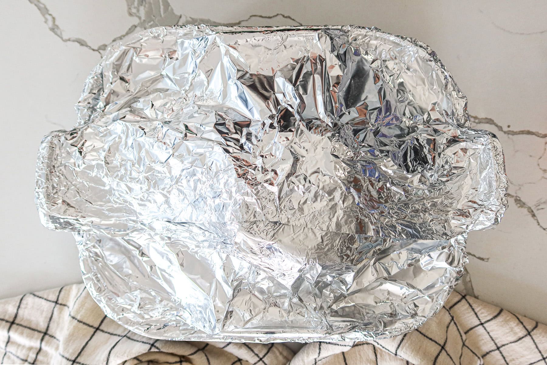 Ham in a roasting pan covered with aluminum foil.