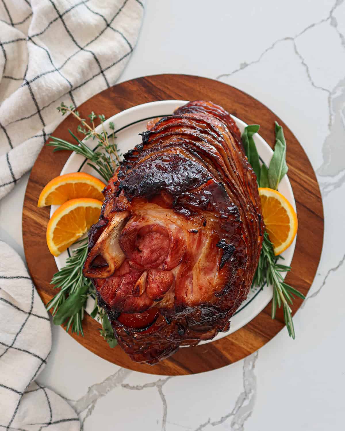 Baked spiral ham on a plate with herb and orange slice garnish.