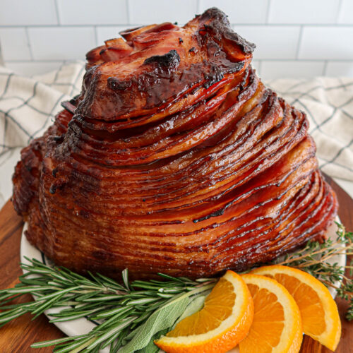 Glazed spiral ham with fresh herb and orange slice garnish.