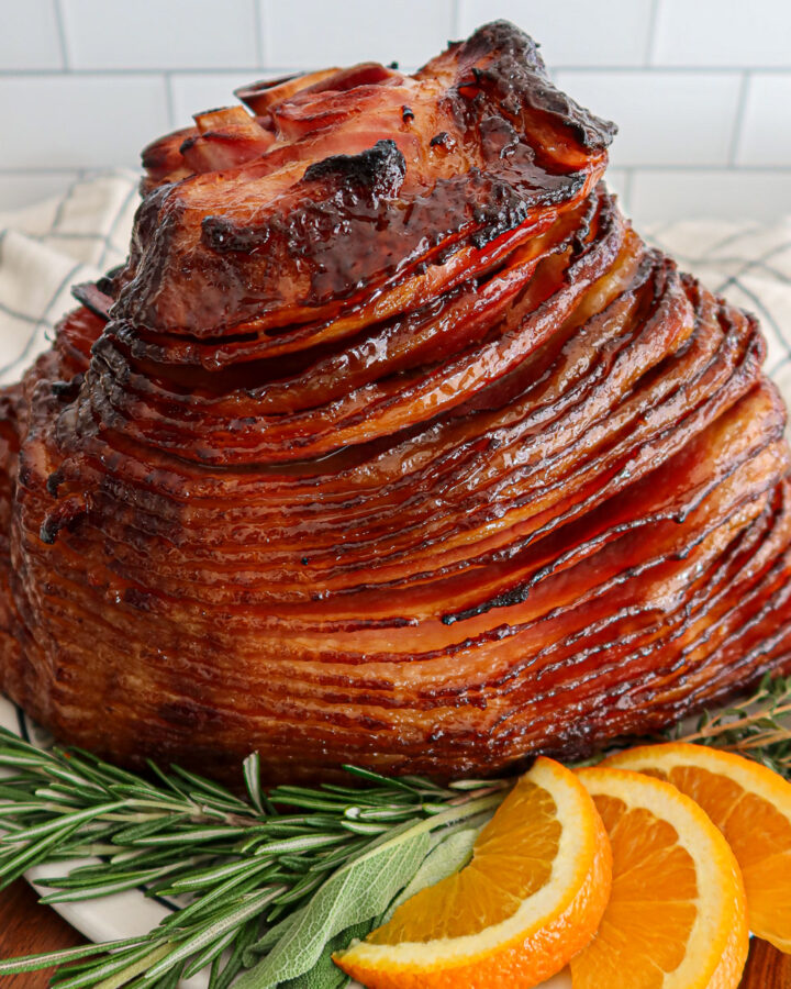 Glazed spiral ham with fresh herb and orange slice garnish.