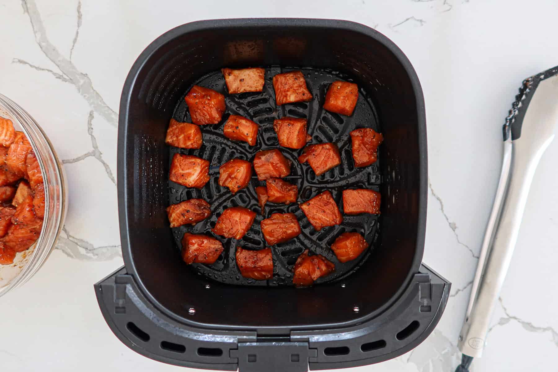Seasoned salmon cubes in air fryer basket.