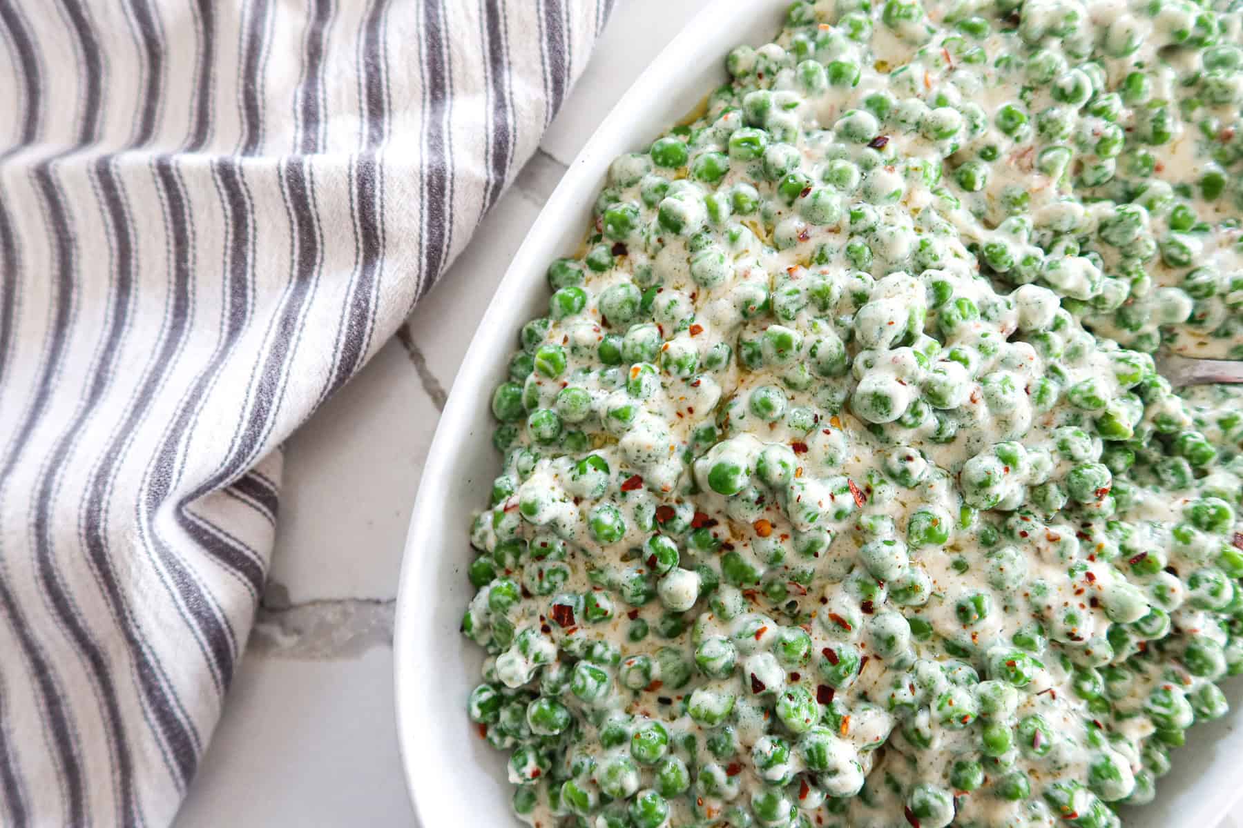 Creamed peas in an oval white serving dish.