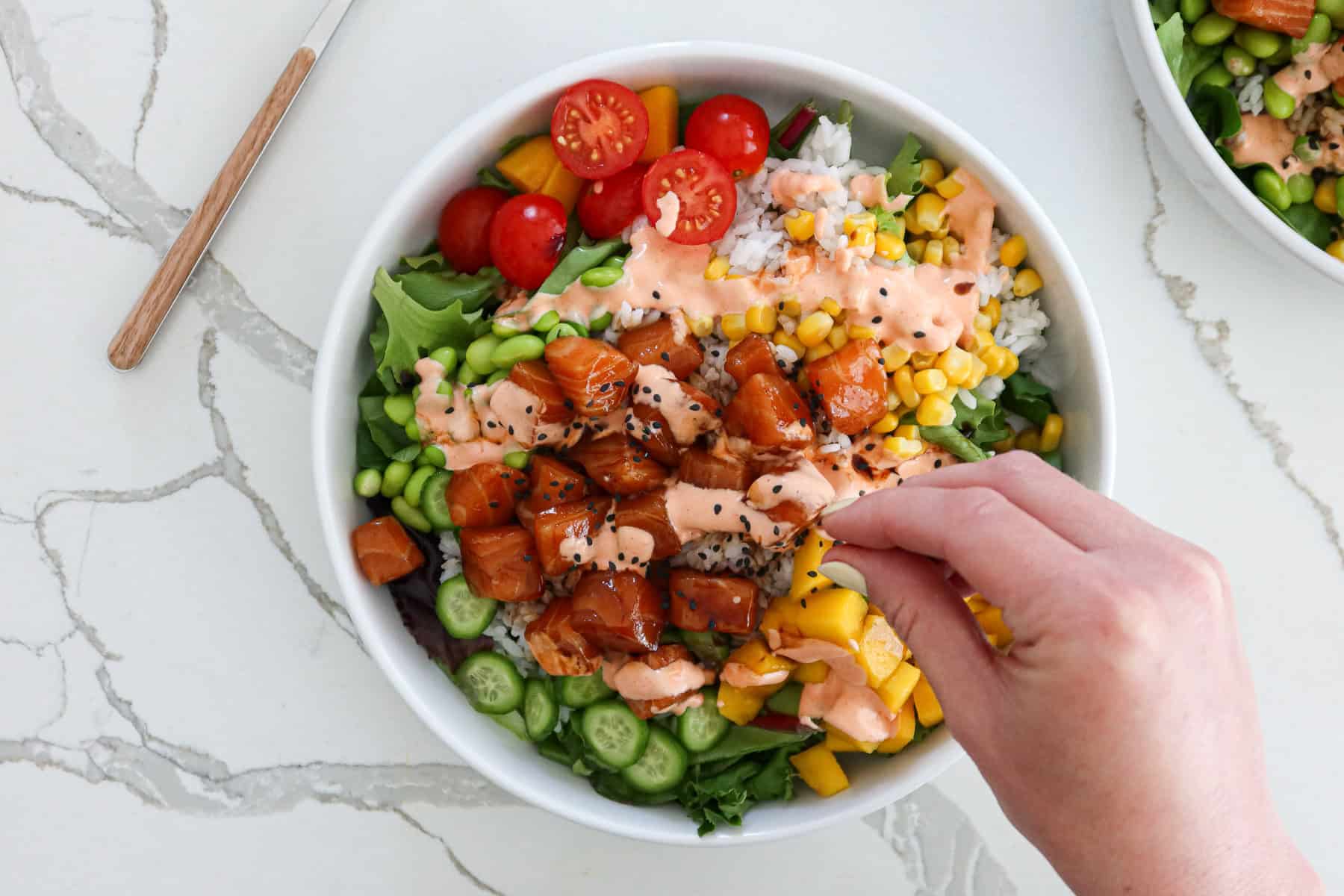 Adding sesame seeds to a salmon poke bowl.