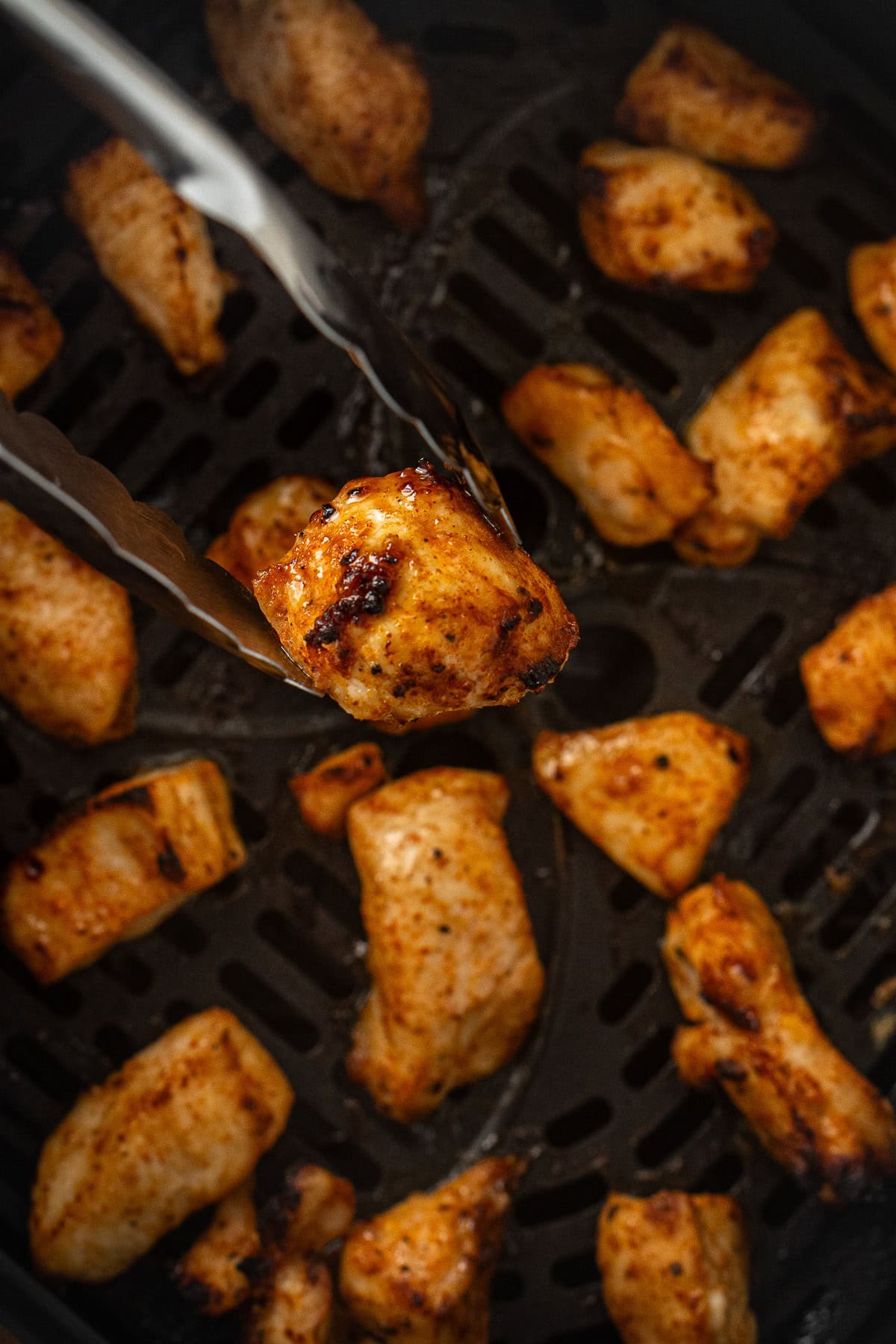Close up of tongs holding an air fryer chicken bite.
