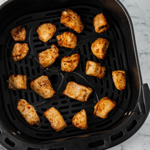 Cooked chicken bites in air fryer basket.