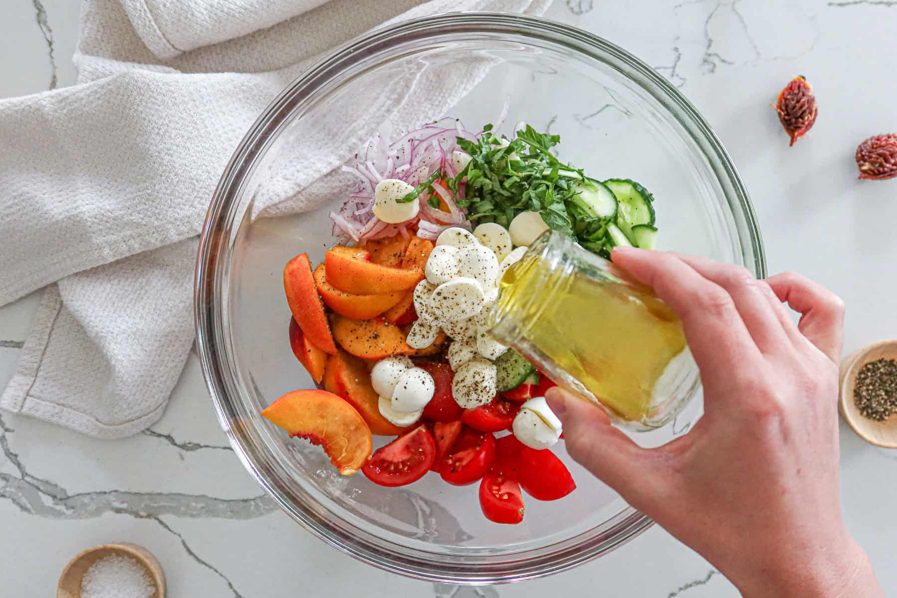 Adding dressing to bowl containing peaches, tomatoes, mozzarella, cucumber, onion, basil and seasonings.