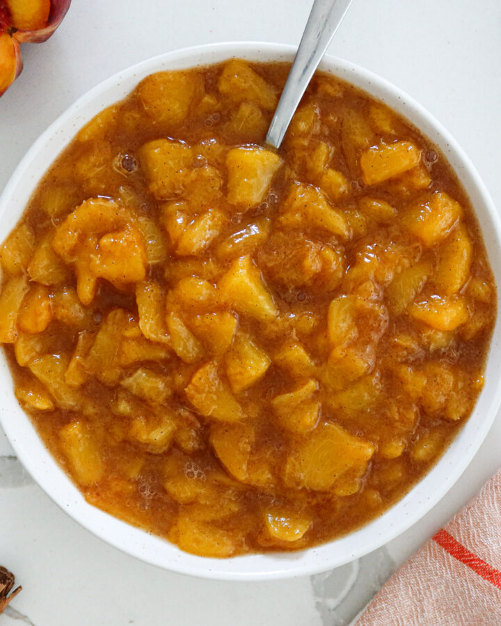 Peach compote in a white bowl with spoon.