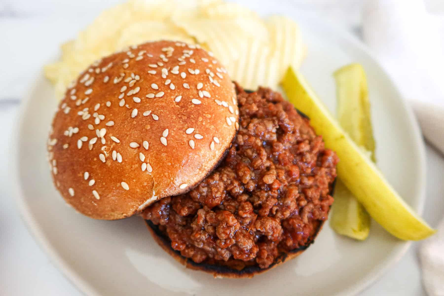 Sloppy joe, pickles and chips on a white plate.