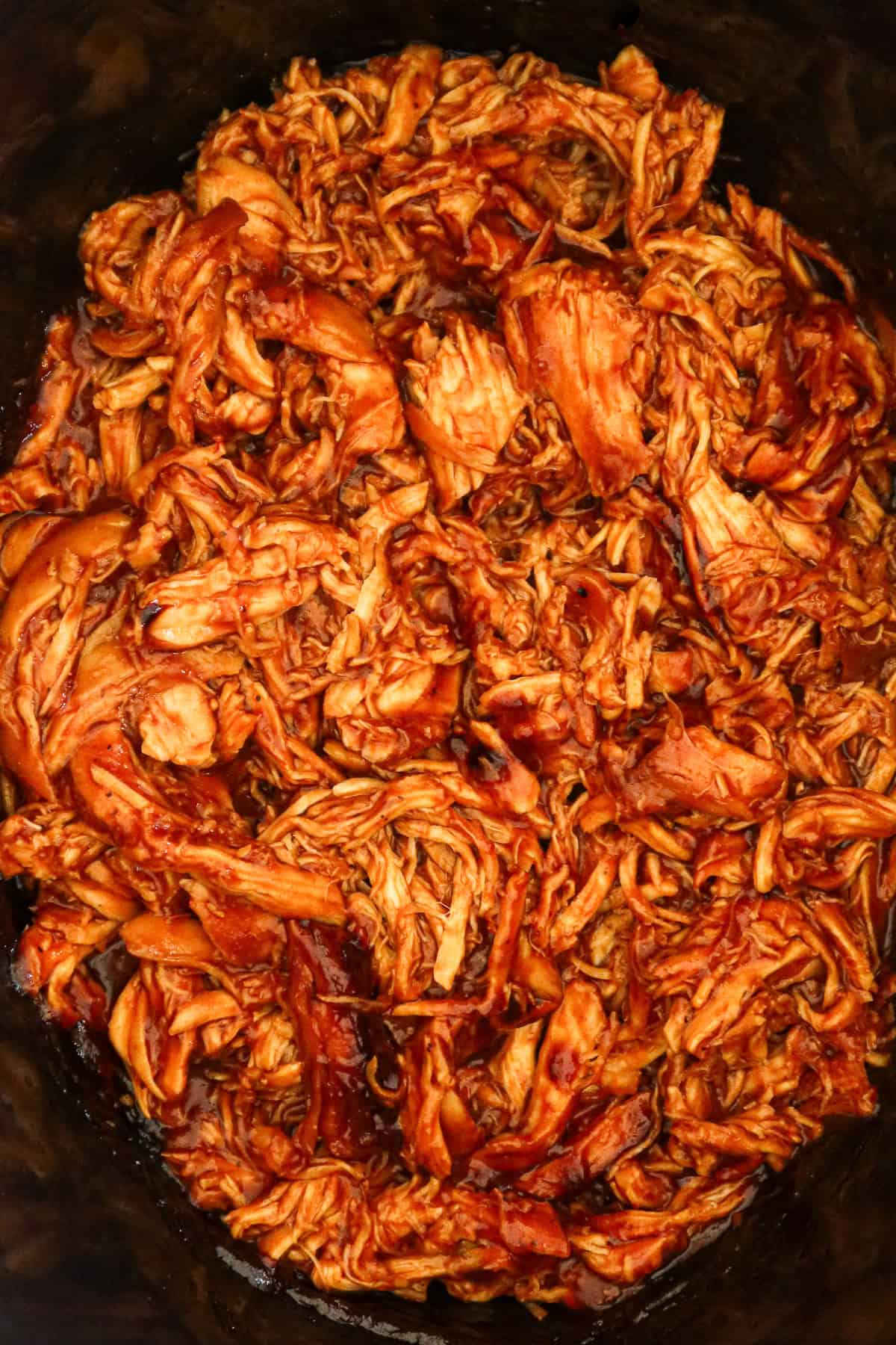 Shredded bbq chicken in black slow cooker.