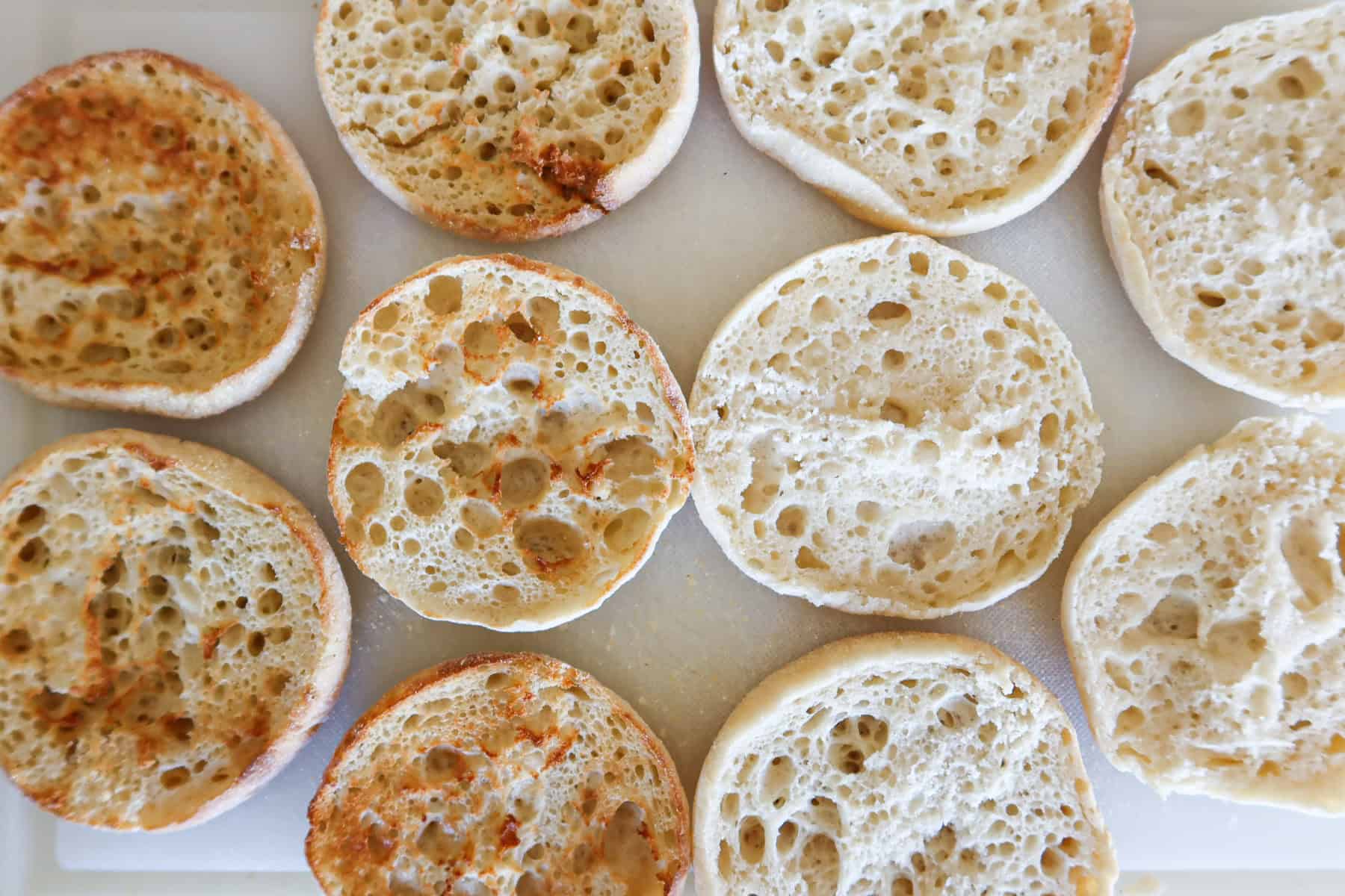 English muffins on a cutting board. Half are pre-toasted and half are not toasted.