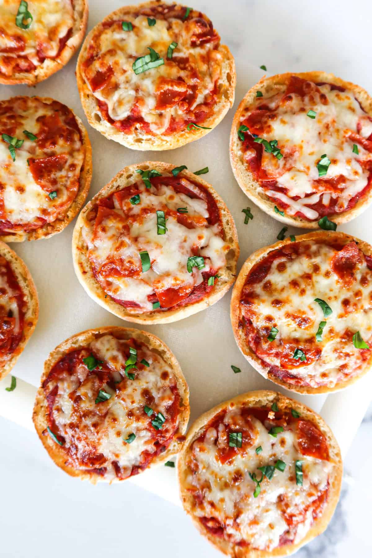English muffin pizzas on a white cutting board.