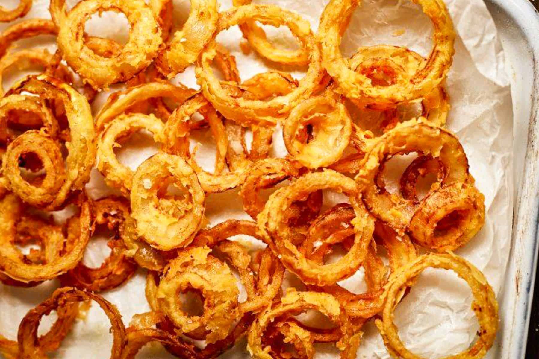 Onion rings on a white baking sheet on top of parchment paper.