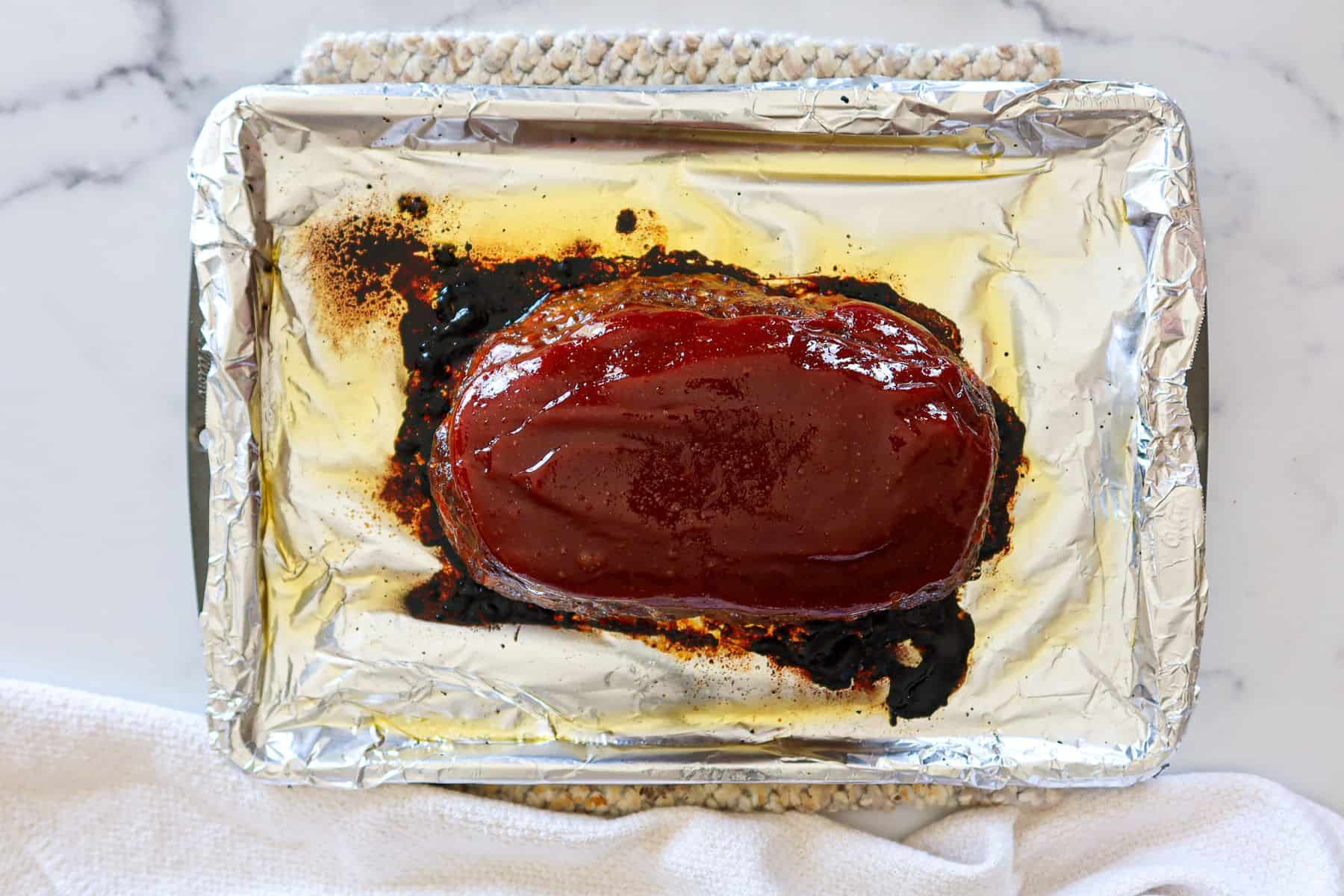 Partially baked meatloaf covered in glaze sauce.