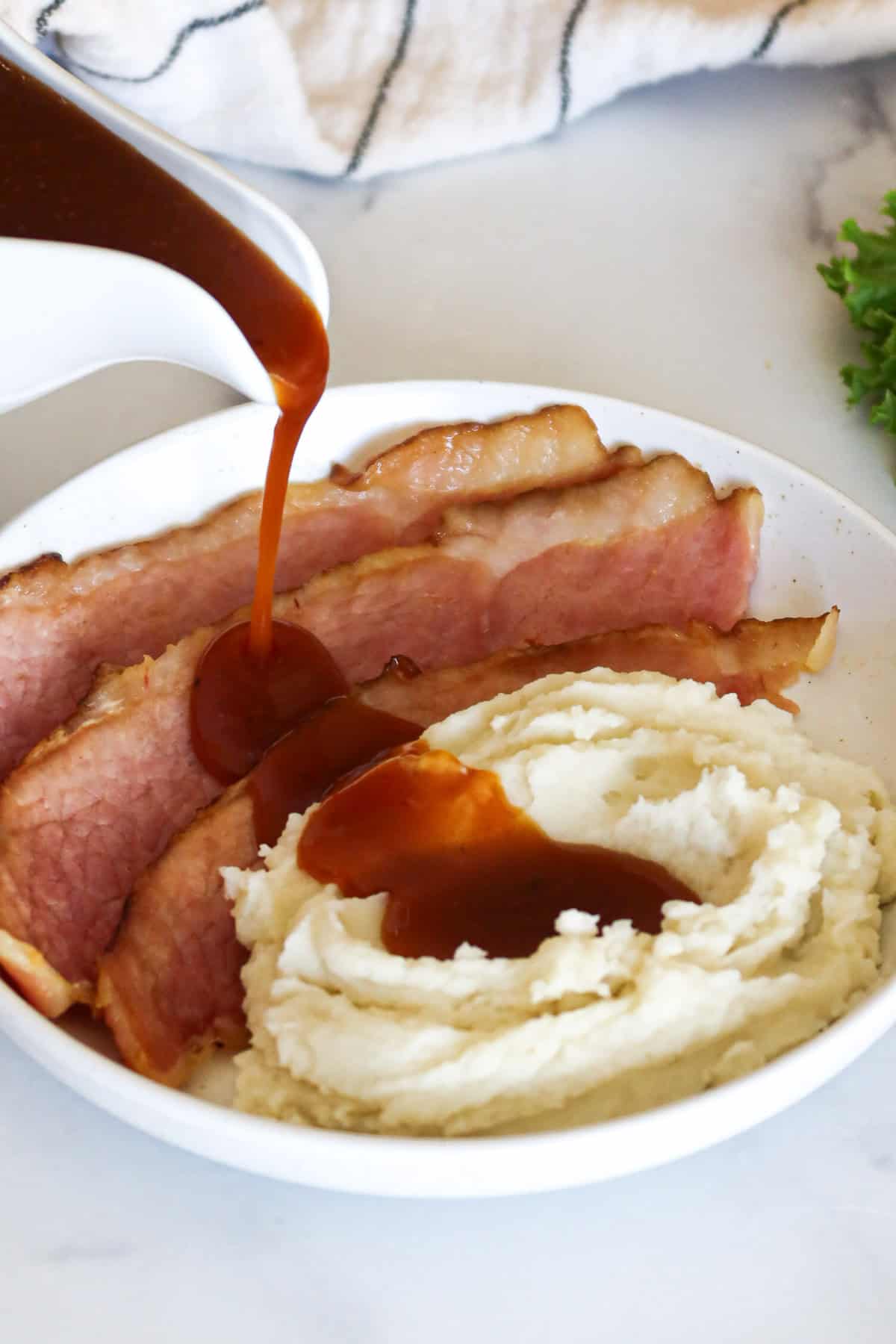 Pouring ham gravy over ham slices and mashed potatoes.