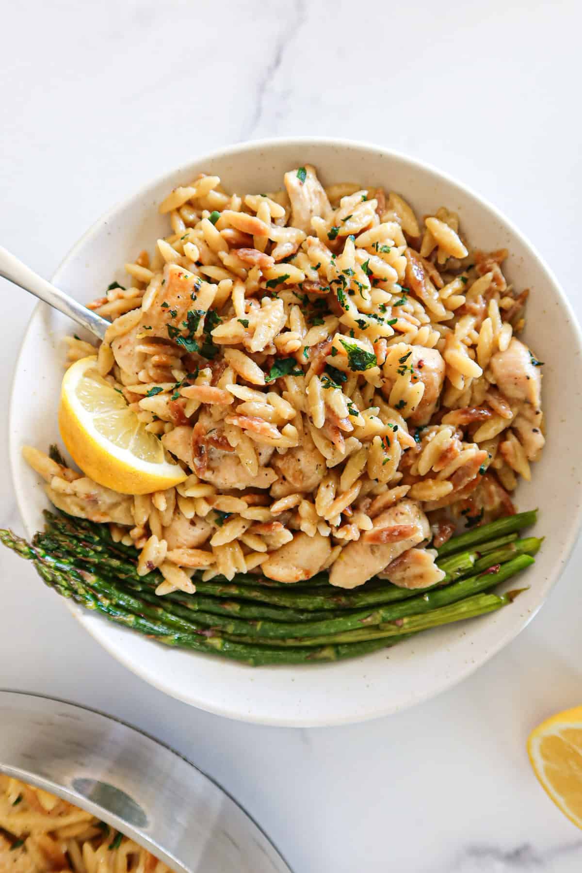 Creamy lemon chicken orzo and asparagus on a white serving plate.