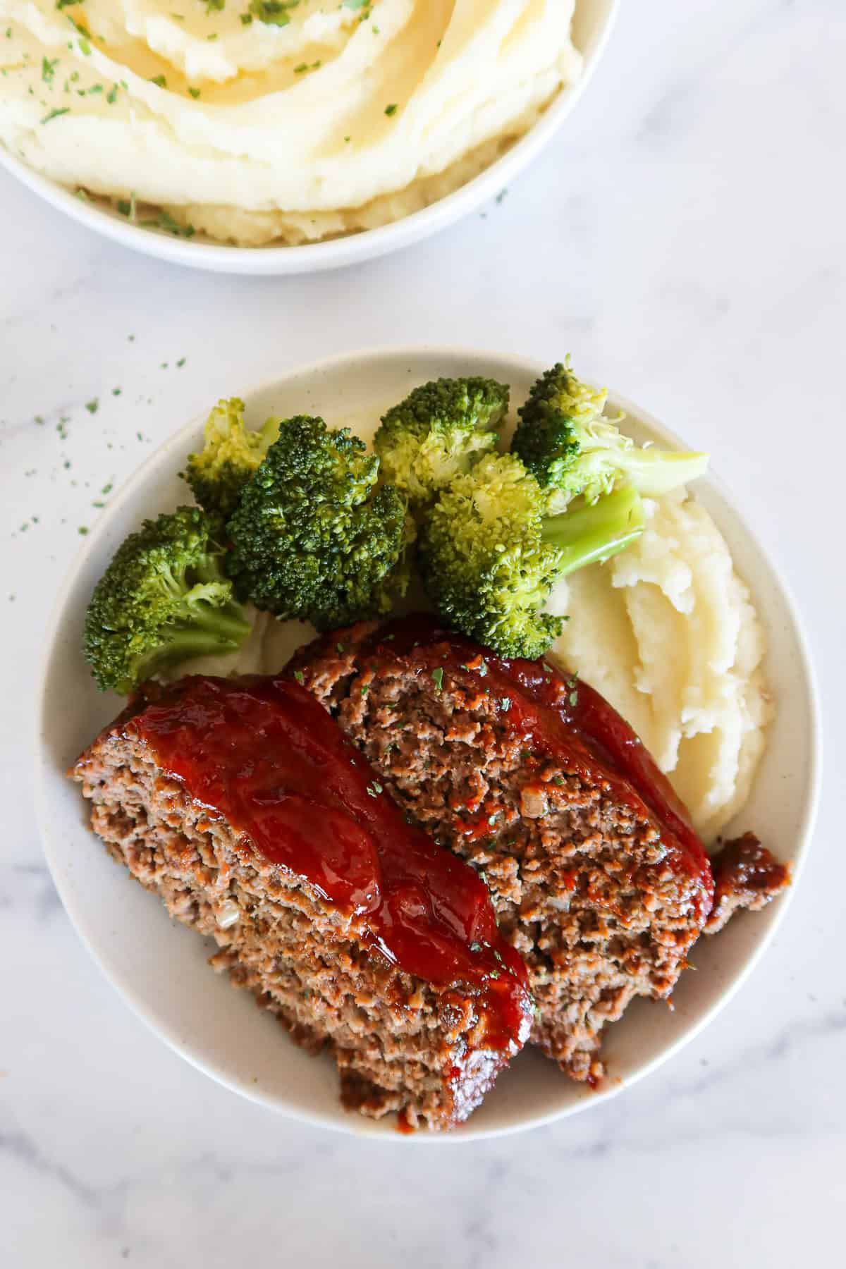 Two slices of eggless meatloaf on a plate with broccoli and mashed potatoes.