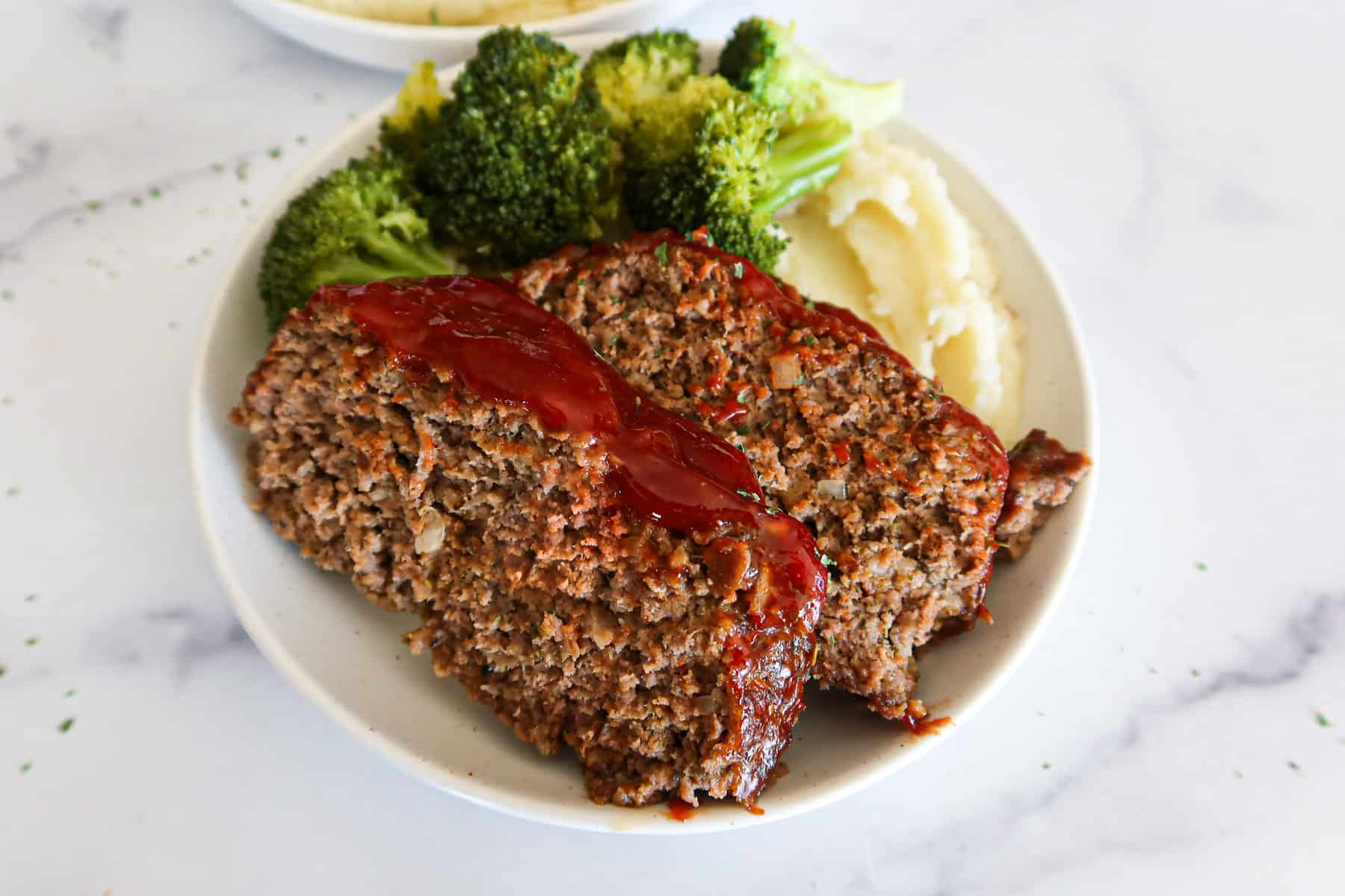 Two slices of eggless meatloaf on a plate with broccoli and mashed potatoes.