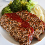 Two slices of egg free meatloaf on a plate with broccoli and mashed potatoes.