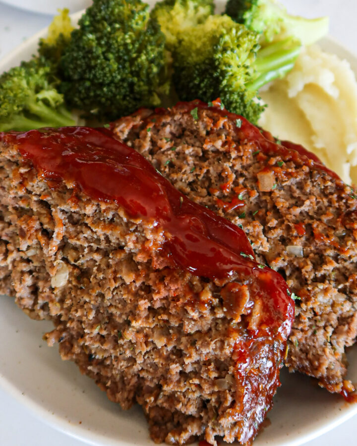 Two slices of egg free meatloaf on a plate with broccoli and mashed potatoes.
