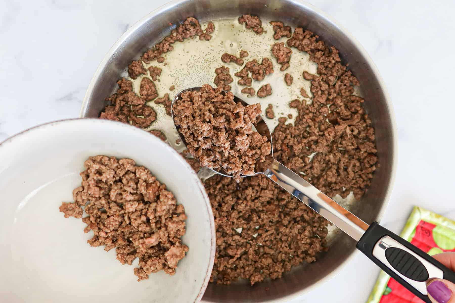 Scooping browned beef into a bowl.