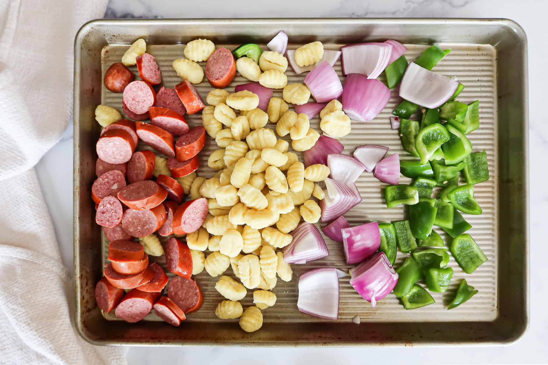 Cut up sausage, gnocchi, red onion and green bell pepper on a sheet pan.