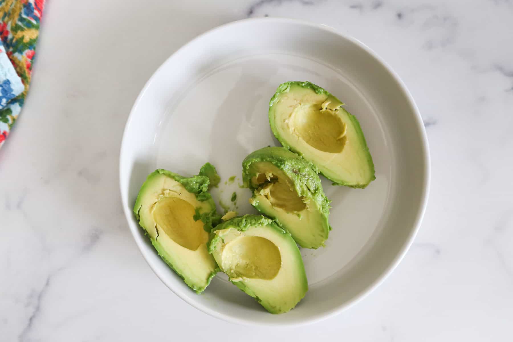 Avocado halves scooped into a bowl.