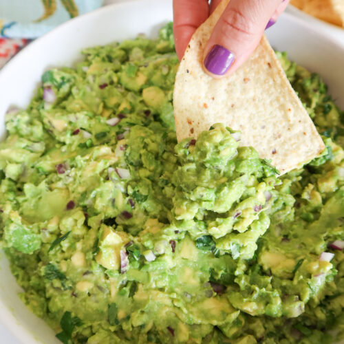 Scooping guacamole with a tortilla chip.