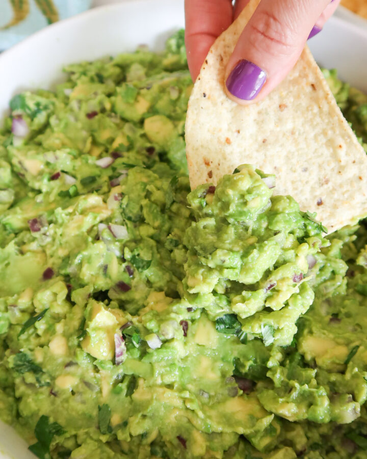 Scooping guacamole with a tortilla chip.