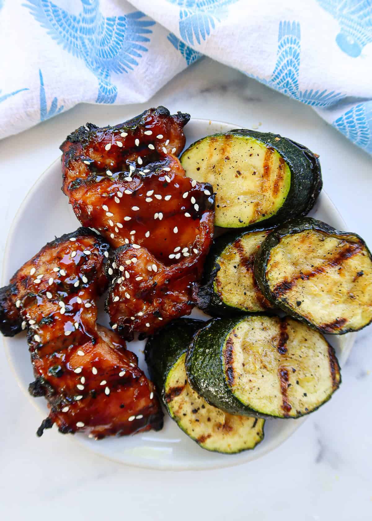 Grilled zucchini and teriyaki grilled chicken on a white plate.