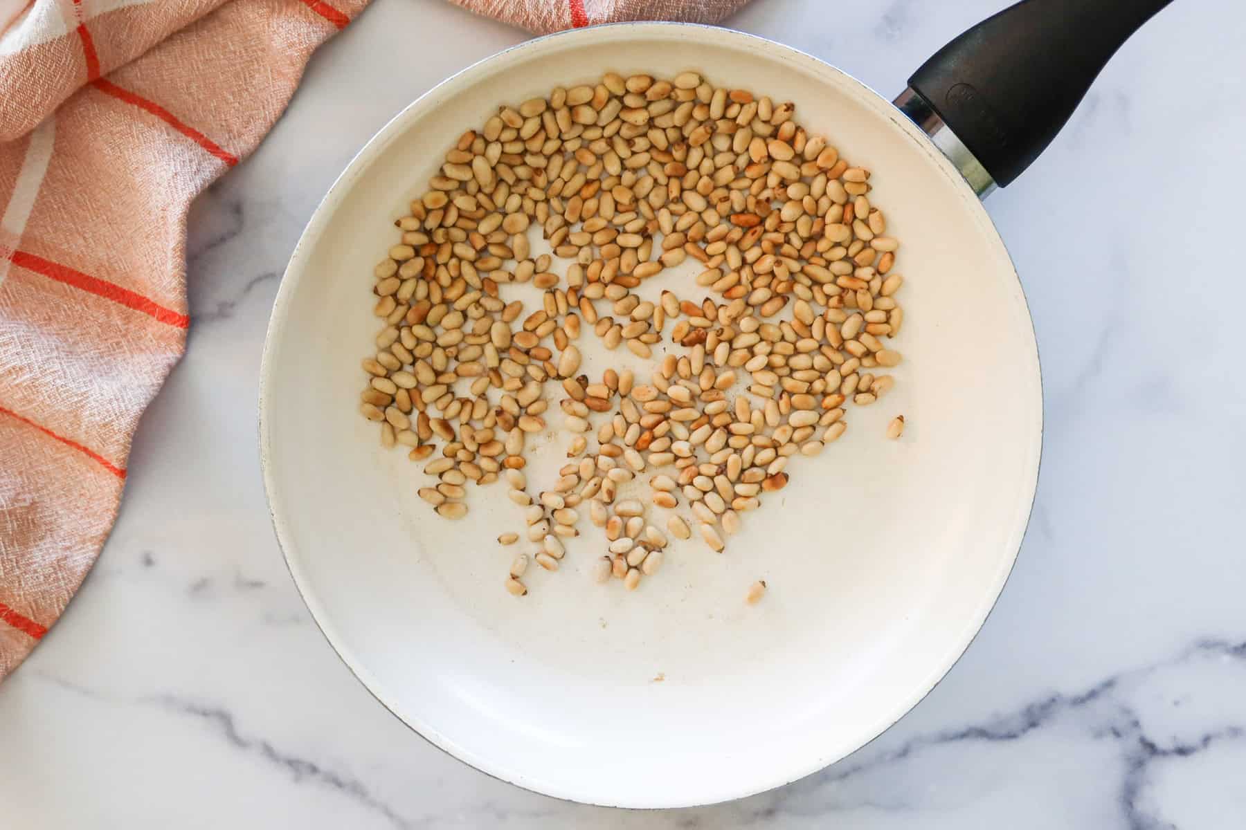 Toasting pine nuts in a white skillet.